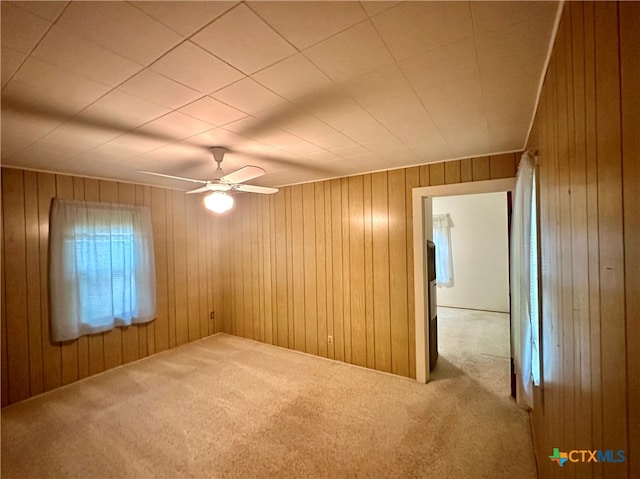 carpeted empty room with wood walls and ceiling fan