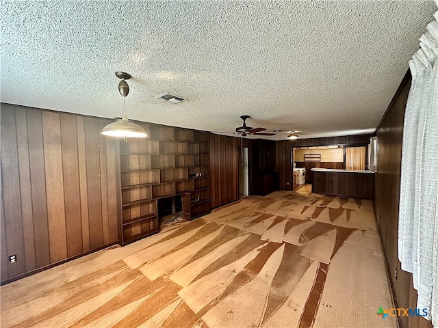 unfurnished living room featuring ceiling fan, wooden walls, and a textured ceiling