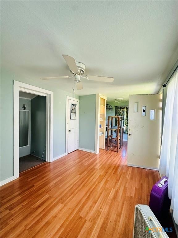 unfurnished living room with light wood-style flooring, a textured ceiling, baseboards, and a ceiling fan