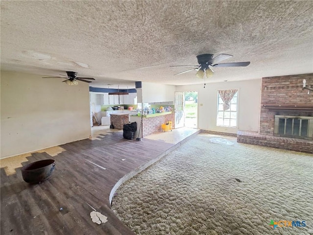 403 Schell Rd, Victoria, TX 77904 - unfurnished living room featuring ceiling fan, a brick fireplace, wood finished floors, and a textured ceiling