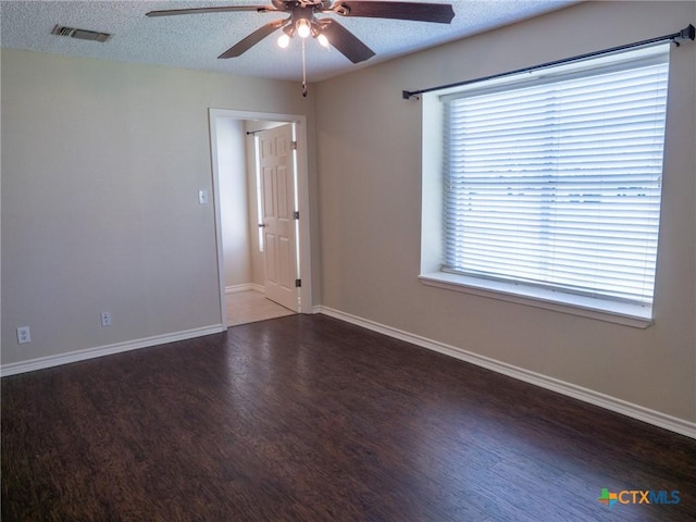 spare room with a textured ceiling, wood finished floors, visible vents, and baseboards