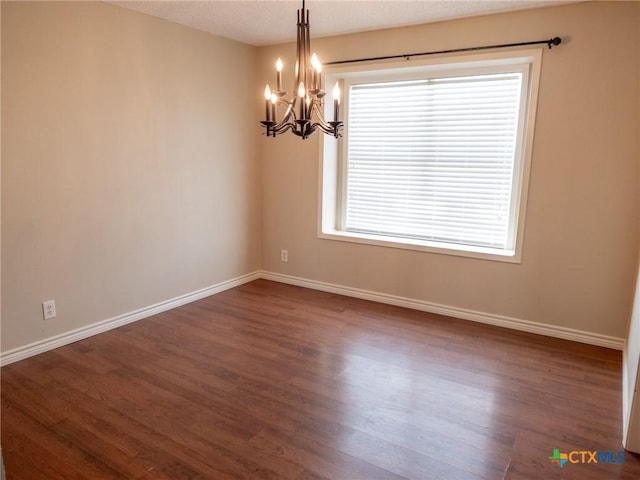 unfurnished room featuring a notable chandelier, dark wood-style flooring, and baseboards