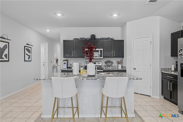 kitchen with appliances with stainless steel finishes, light stone counters, and an island with sink