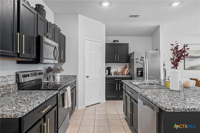 kitchen with stainless steel appliances, dark stone counters, light tile patterned floors, sink, and a kitchen island with sink