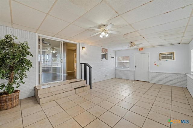 interior space with a ceiling fan, a paneled ceiling, an AC wall unit, and brick wall