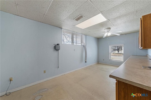 interior space with a paneled ceiling, baseboards, visible vents, and a ceiling fan