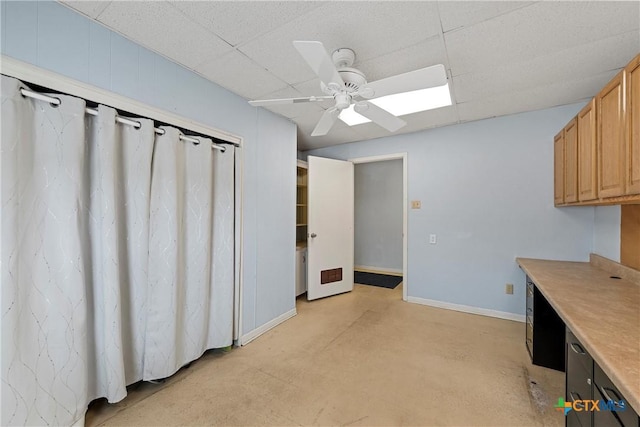 interior space featuring baseboards, a ceiling fan, concrete flooring, and a drop ceiling