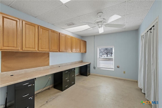 unfurnished office featuring ceiling fan, built in desk, visible vents, and a paneled ceiling