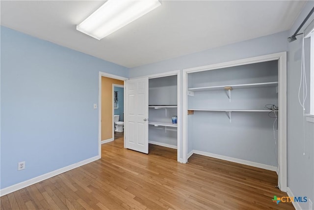 unfurnished bedroom with baseboards, light wood-type flooring, and multiple closets