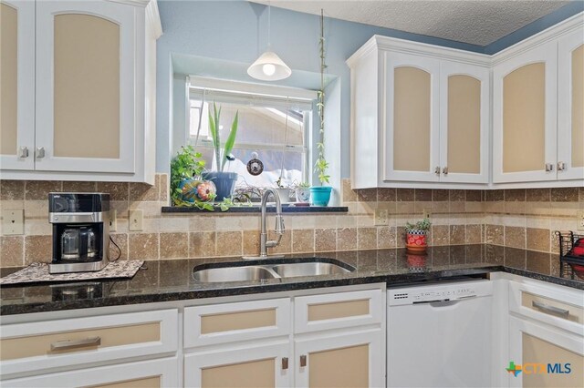 kitchen featuring white dishwasher, a sink, dark stone countertops, tasteful backsplash, and white cabinets