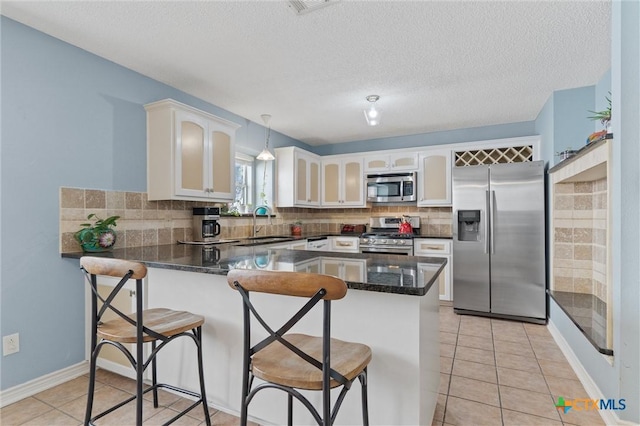 kitchen featuring stainless steel appliances, a peninsula, backsplash, light tile patterned flooring, and white cabinets