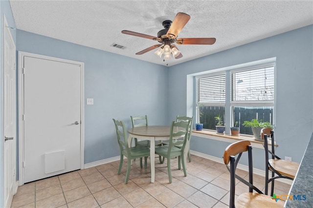 dining space with a textured ceiling, ceiling fan, baseboards, and light tile patterned flooring