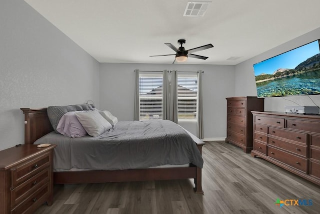 bedroom featuring ceiling fan, visible vents, baseboards, and wood finished floors