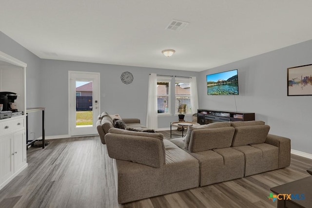 living area featuring wood finished floors, a healthy amount of sunlight, visible vents, and baseboards