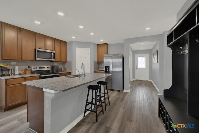 kitchen featuring light wood-type flooring, brown cabinets, a sink, a kitchen breakfast bar, and stainless steel appliances