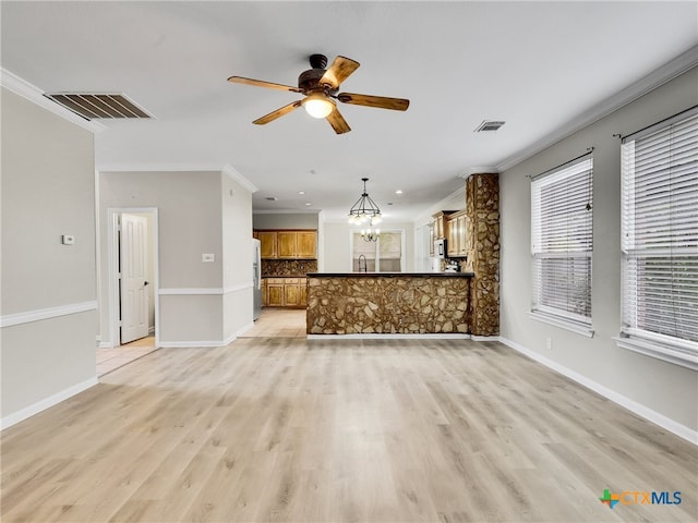 unfurnished living room with ceiling fan with notable chandelier, light hardwood / wood-style flooring, and crown molding