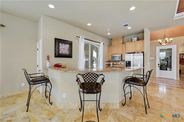 kitchen featuring appliances with stainless steel finishes, light brown cabinetry, a breakfast bar, pendant lighting, and an inviting chandelier