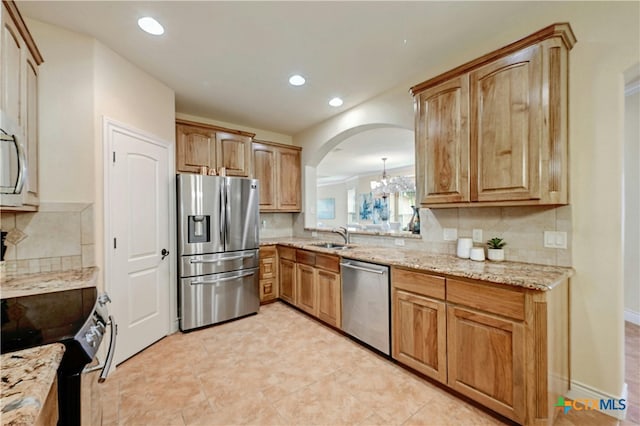 kitchen featuring backsplash, an inviting chandelier, sink, light stone countertops, and stainless steel appliances