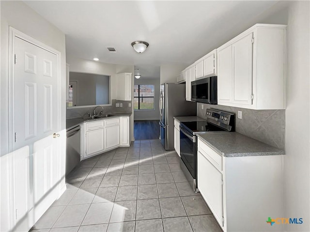 kitchen with appliances with stainless steel finishes, tasteful backsplash, sink, white cabinetry, and light tile patterned flooring