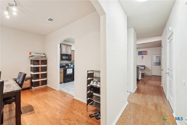 hall featuring visible vents, light wood-style floors, arched walkways, and baseboards