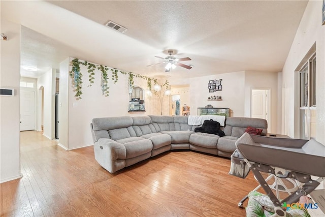 living area featuring visible vents, a ceiling fan, a textured ceiling, light wood-style floors, and baseboards