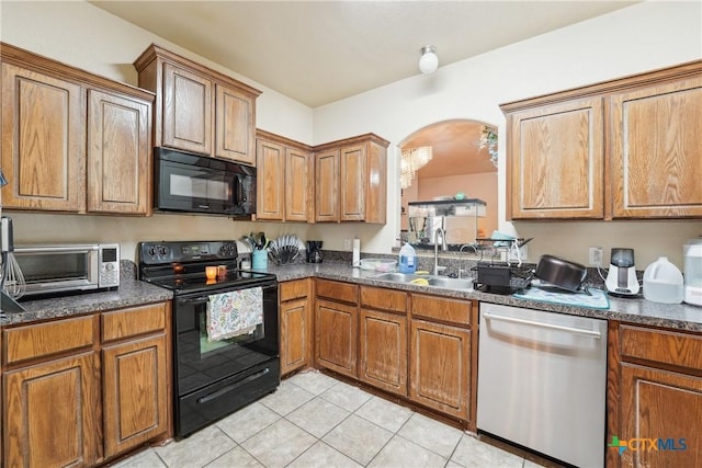 kitchen with black appliances, a sink, dark countertops, arched walkways, and light tile patterned floors