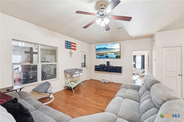 living room with visible vents, a textured ceiling, wood finished floors, and a ceiling fan