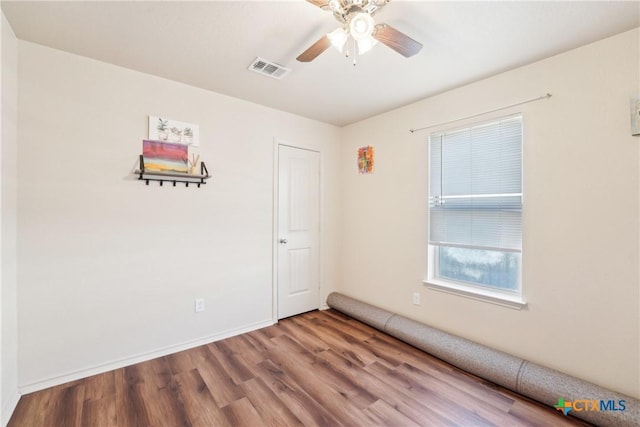 unfurnished room featuring a ceiling fan, visible vents, wood finished floors, and baseboards