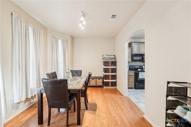 dining area with baseboards, light wood-style floors, visible vents, and arched walkways