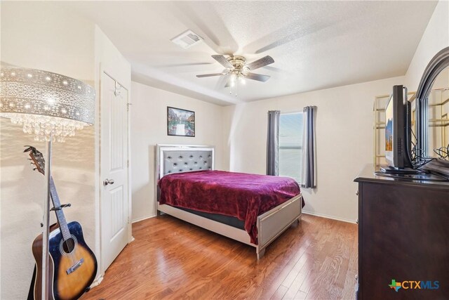 bedroom with a ceiling fan, wood finished floors, visible vents, and baseboards