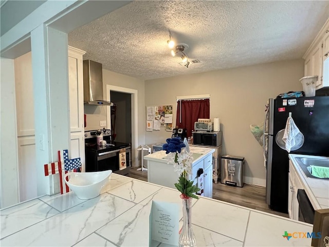 1308 E Park Ave, Victoria, TX 77901 - kitchen featuring wall chimney exhaust hood, a textured ceiling, a kitchen island, appliances with stainless steel finishes, and white cabinetry