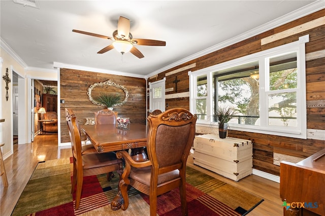 dining area featuring ceiling fan, wood-type flooring, wooden walls, and crown molding