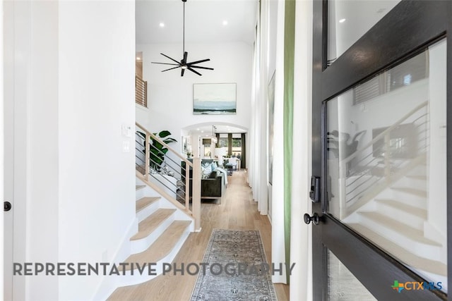 foyer entrance featuring wood finished floors, stairs, arched walkways, a high ceiling, and ceiling fan