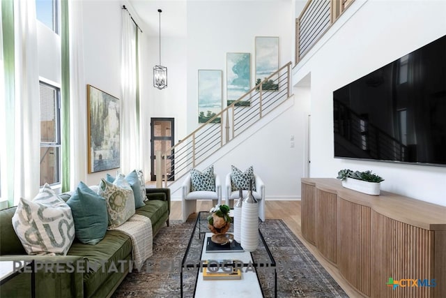 living room with a towering ceiling, stairs, wood finished floors, baseboards, and a chandelier
