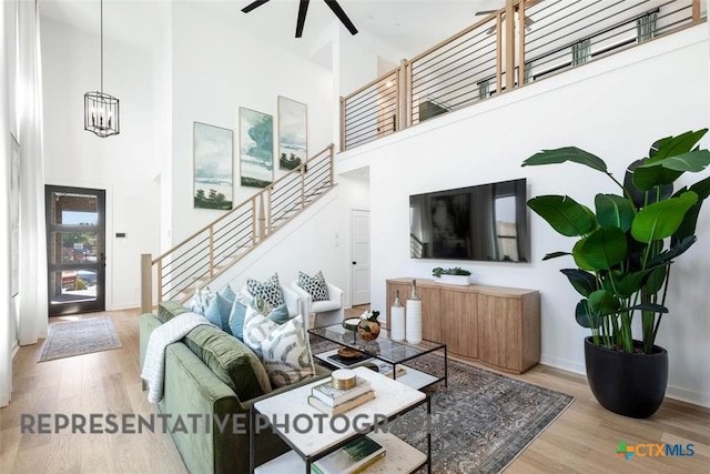 living room with stairs, a high ceiling, wood finished floors, a ceiling fan, and a chandelier