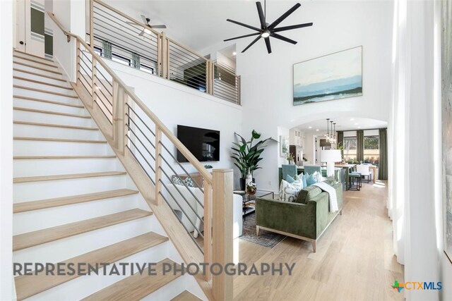 living area featuring a high ceiling, a ceiling fan, stairs, light wood finished floors, and arched walkways