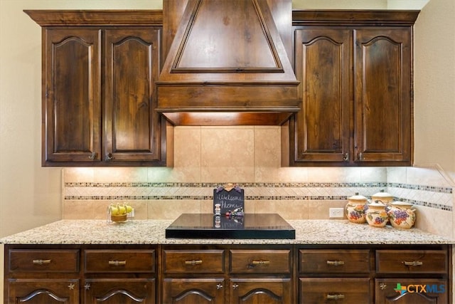 kitchen with light stone counters, premium range hood, black electric stovetop, dark brown cabinets, and tasteful backsplash