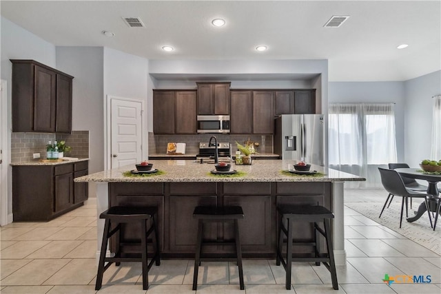 1433 Kamryn Way, New Braunfels, TX 78130 - kitchen with appliances with stainless steel finishes, dark brown cabinets, backsplash, light stone counters, and a center island with sink