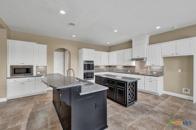 2194 Ranch Loop Dr, New Braunfels, TX 78132 - kitchen with a kitchen island with sink, stainless steel appliances, arched walkways, tasteful backsplash, and light stone countertops