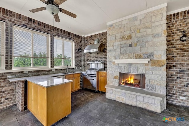 2194 Ranch Loop Dr, New Braunfels, TX 78132 - kitchen with wall chimney range hood, stainless steel stove, a ceiling fan, a peninsula, and a fireplace