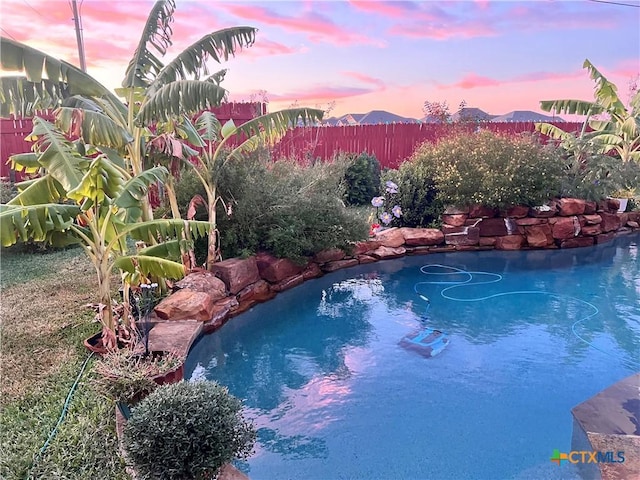 pool at dusk with fence, a mountain view, and a fenced in pool