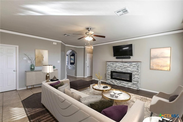 tiled living room featuring a fireplace, visible vents, arched walkways, and ornamental molding