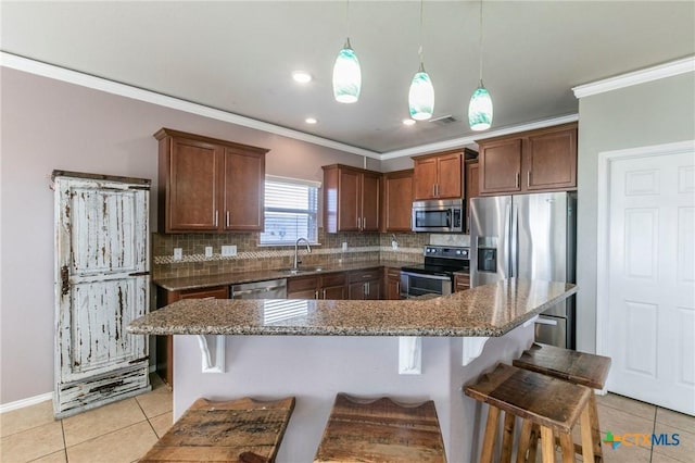 kitchen with a breakfast bar area, stainless steel appliances, a sink, hanging light fixtures, and backsplash