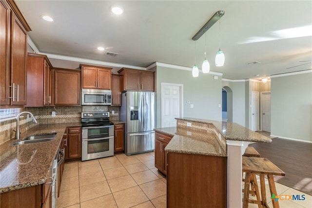 kitchen with a kitchen island, appliances with stainless steel finishes, brown cabinets, a kitchen bar, and a sink