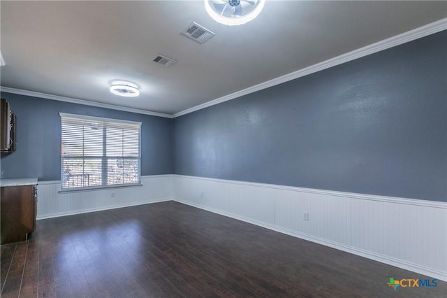 empty room featuring dark wood-type flooring, wainscoting, visible vents, and crown molding