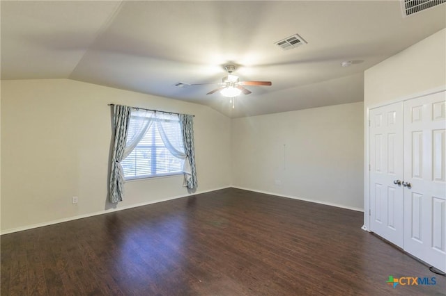 spare room featuring dark wood-style floors, visible vents, and vaulted ceiling