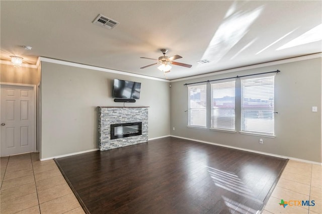 unfurnished living room with ceiling fan, a stone fireplace, visible vents, and crown molding