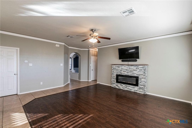 unfurnished living room with visible vents, arched walkways, ceiling fan, crown molding, and a stone fireplace