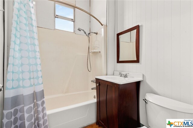 full bathroom featuring wood walls, vanity, toilet, and shower / tub combo