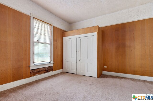 unfurnished bedroom featuring wood walls, multiple windows, and light colored carpet